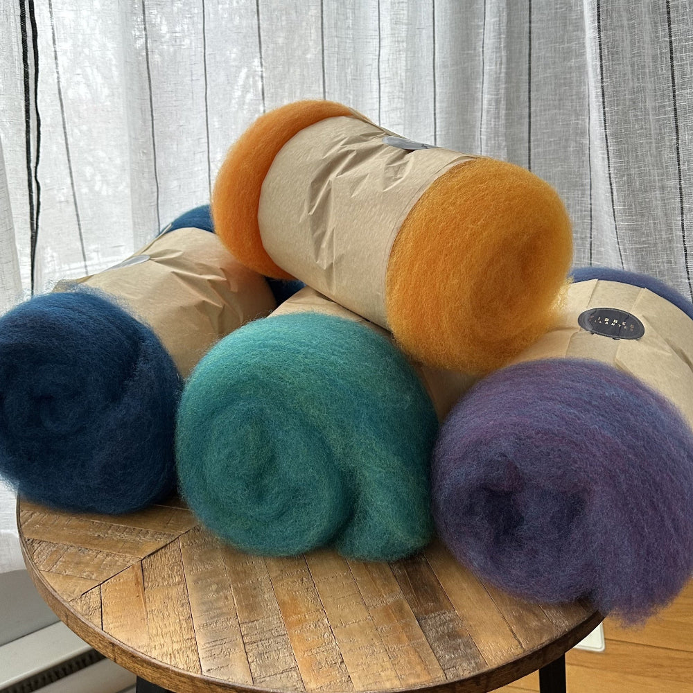 Five balls of yarn in different colors on a wooden table with a neutral background
